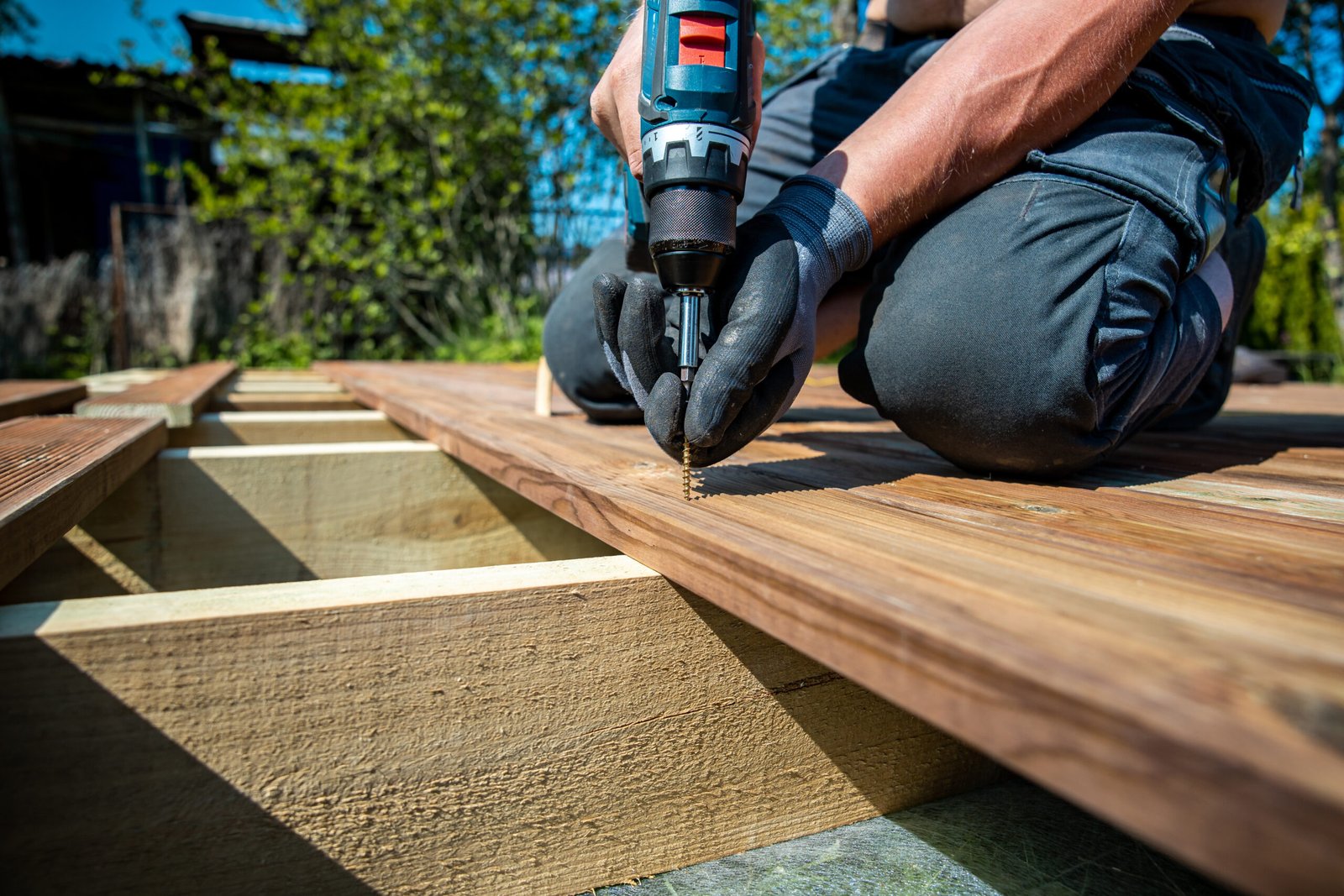 deck construction builder hand with electric screwdriver installing impregnated wooden boards scaled